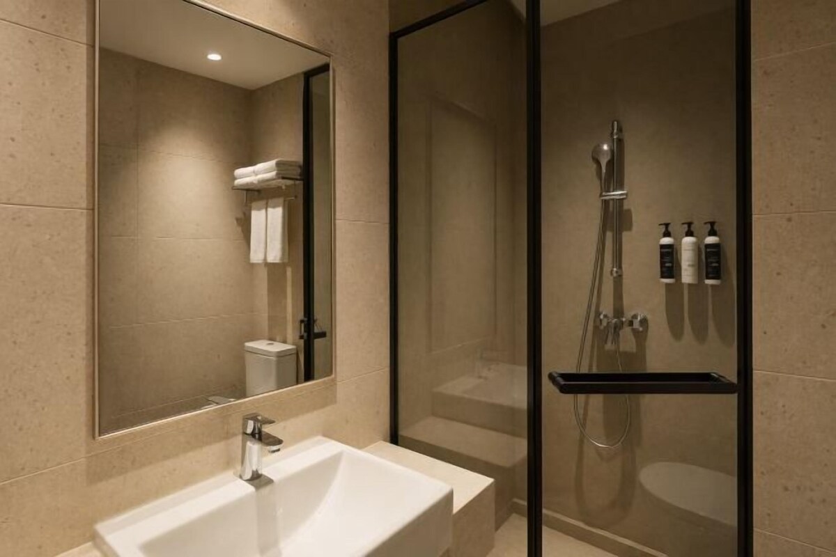 A modern bathroom with a large mirror, a sink, a shower enclosure, and toiletries on a shelf.