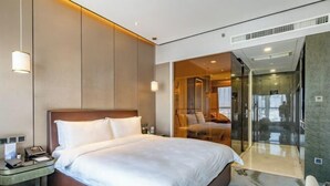 Une chambre d’hôtel moderne avec un grand lit, une table de chevet, une cloison en verre et une vue sur l’intérieur de la pièce.