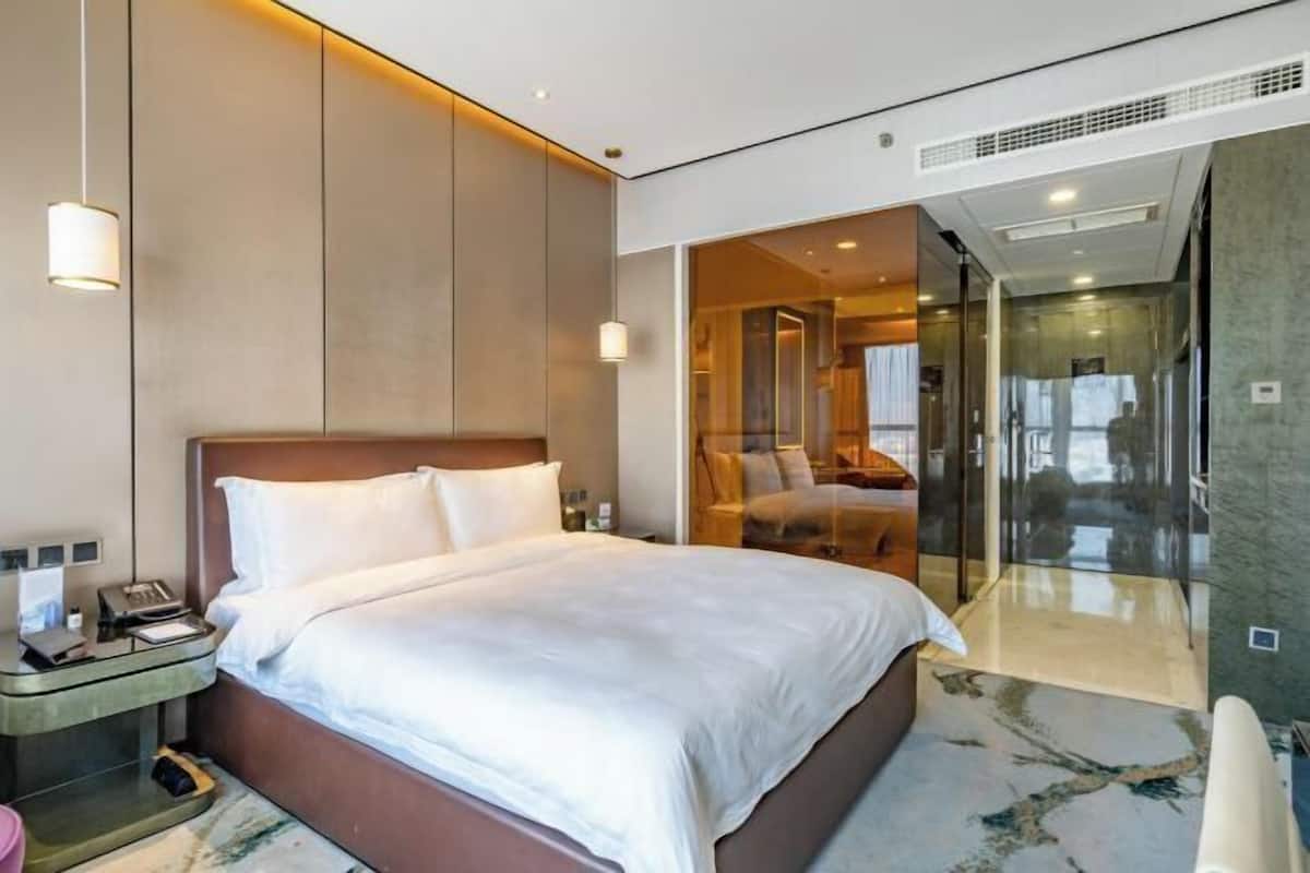Een moderne hotelkamer met een groot bed, een nachtkastje, een glazen scheidingswand en uitzicht op de kamer.