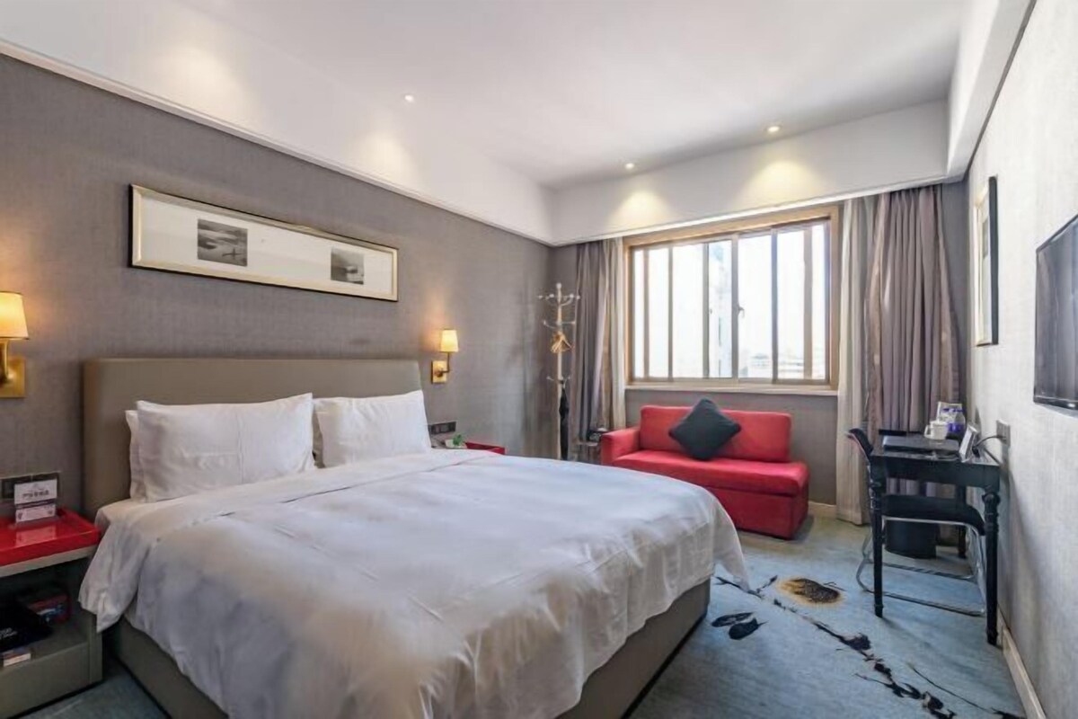 A hotel room with a bed, a red sofa, a desk, and a window with curtains.
