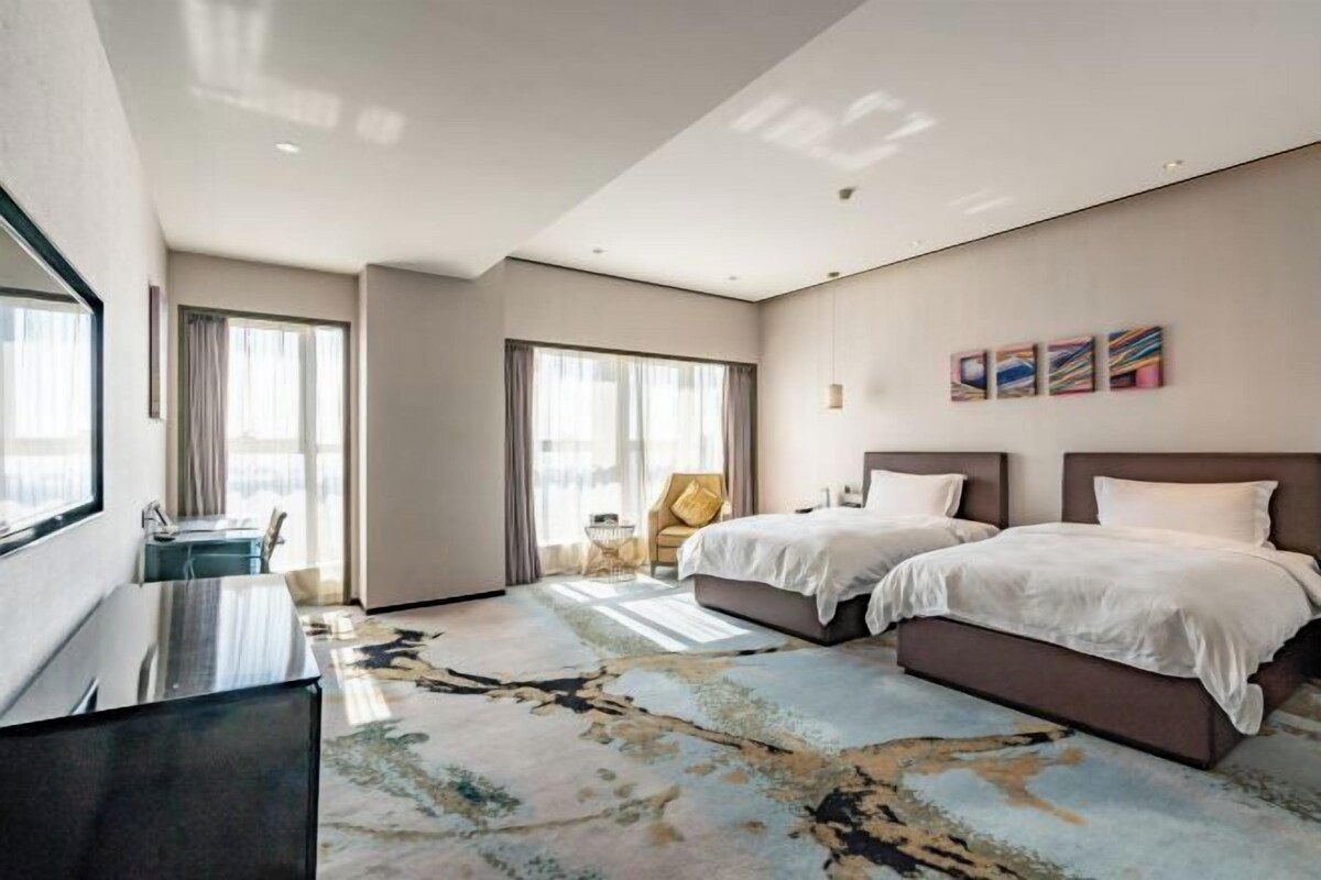 A hotel room with two beds, a desk, a chair, and artwork on the wall.