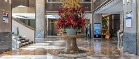 A lobby with a marble floor, a central decorative fountain, and a staircase to the left.