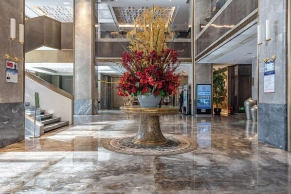 A lobby with a marble floor, a central decorative fountain, and a staircase to the left.