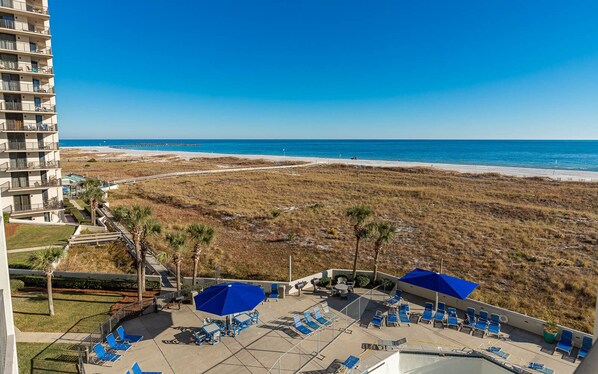 Un hotel frente a la playa con zona de piscina, sillas de descanso y vistas a la playa y al océano.