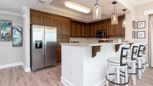 Eine moderne Küche mit Holzschränken, einem Edelstahlkühlschrank, einer Mikrowelle und einer Bar mit weißen Barhocker.