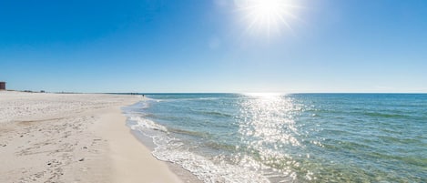 A beach with clear water, a sandy shore, and a bright sun.