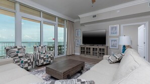 Ein geräumiges Wohnzimmer mit großem Flachbildfernseher, bequemen Sitzgelegenheiten und einem Balkon mit Meerblick.