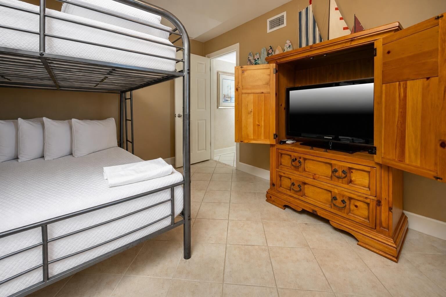 Un lit superposé avec un téléviseur à écran plat placé dans un meuble en bois, une porte et un sol carrelé.