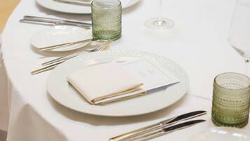 Una mesa servida con platos blancos, cubiertos y vasos de vidrio verde.