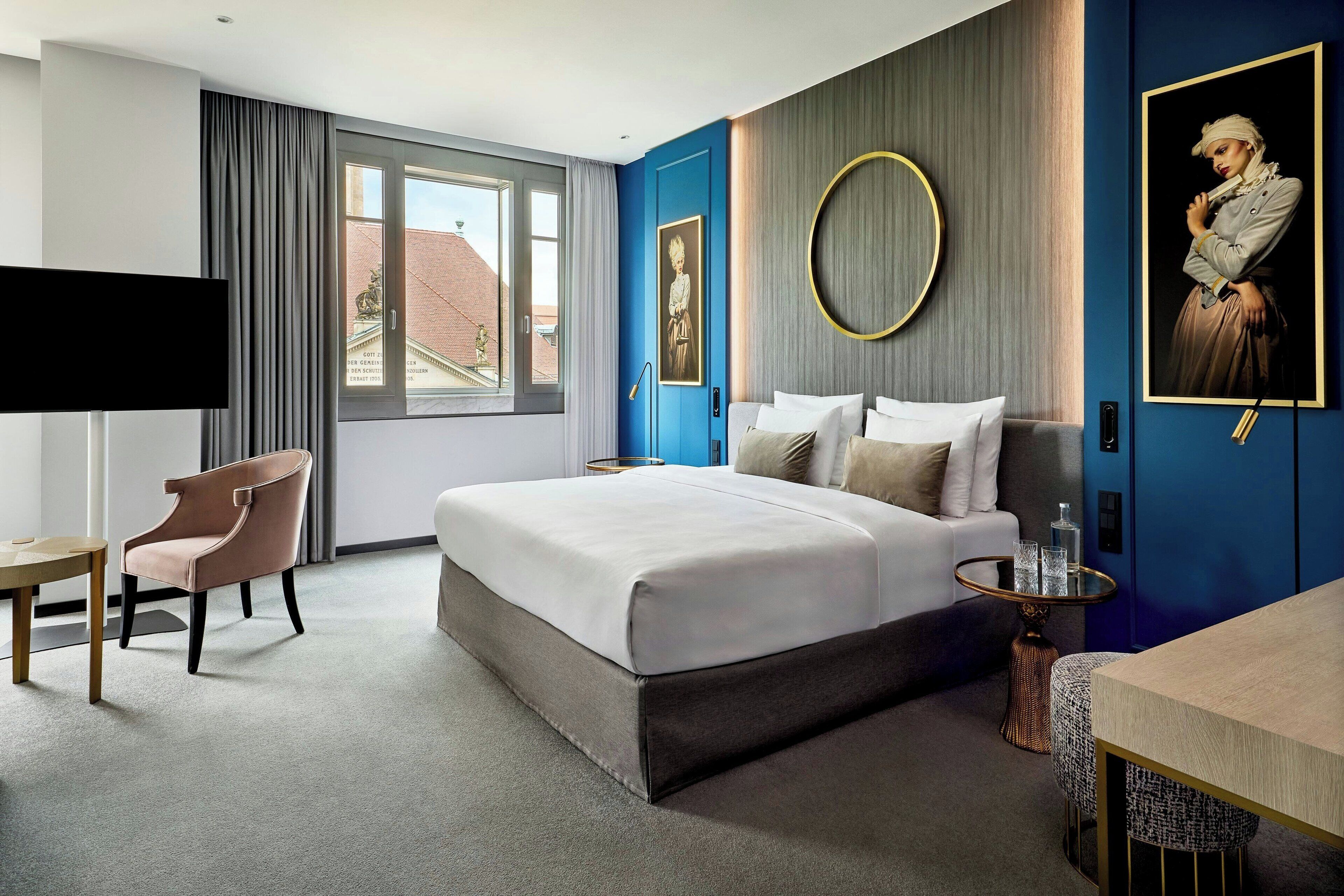 A modern hotel room with a large bed, a desk, a chair, and a TV.