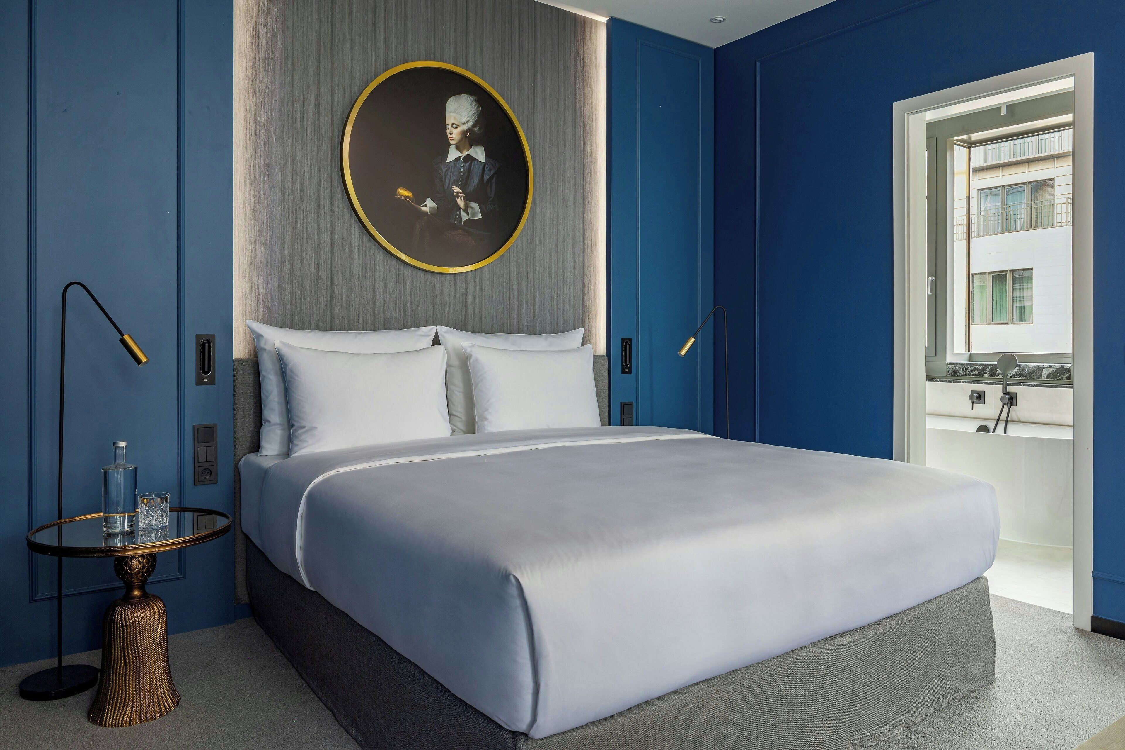 A modern bedroom with a large bed, a round portrait, and a view of a building through a window.
