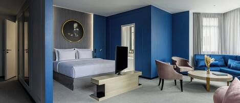 Una habitación de hotel moderna con cama, televisión, zona de estar y un amplio ventanal.