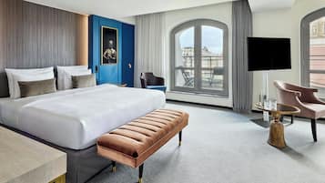 Una habitación de hotel moderna con una cama grande, un banco, una mesa redonda y un televisor.