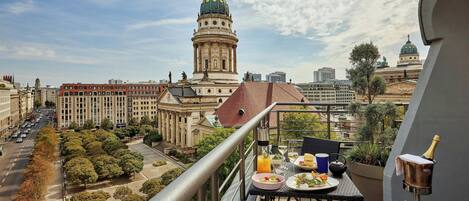 Un balcón con una mesa dispuesta para una comida, con vistas a un paisaje urbano con edificios históricos y una estructura cúpula destacada.