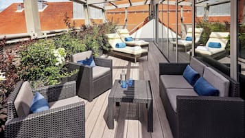 En tagterrasse med fletningsmøbler, puder og et glasindhegning.