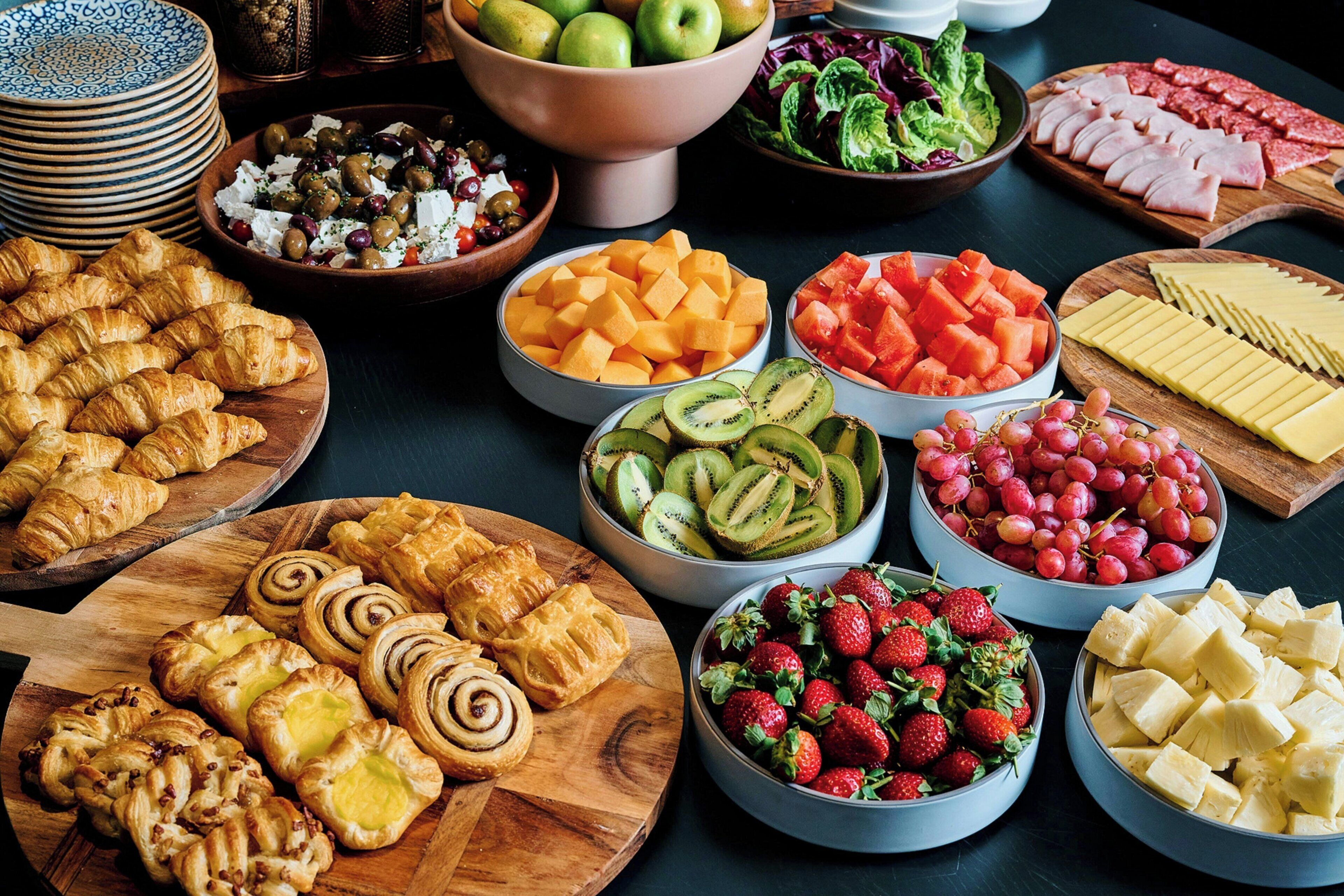 Diverses menes de menjar, com fruita, formatges i pastissos, disposats sobre una taula.