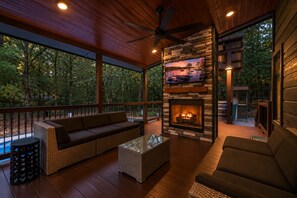 A covered deck with a stone fireplace, wicker furniture, and a television mounted on the wall. - Perfect for Family Gatherings, 4 King Suites, Heated Pool & Fire Pit (Broken Bow)