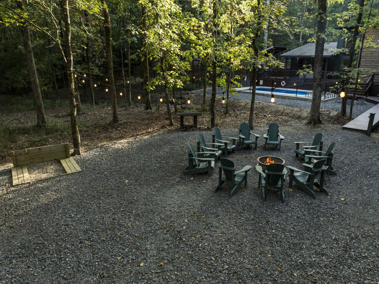 Un espace extérieur aménagé avec des chaises Adirondack disposées autour d’un foyer central, le tout entouré d’arbres et recouvert d’un sol en gravier.