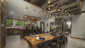 Un'ampia sala da pranzo con un lungo tavolo di legno, diverse sedie e un moderno lampadario.