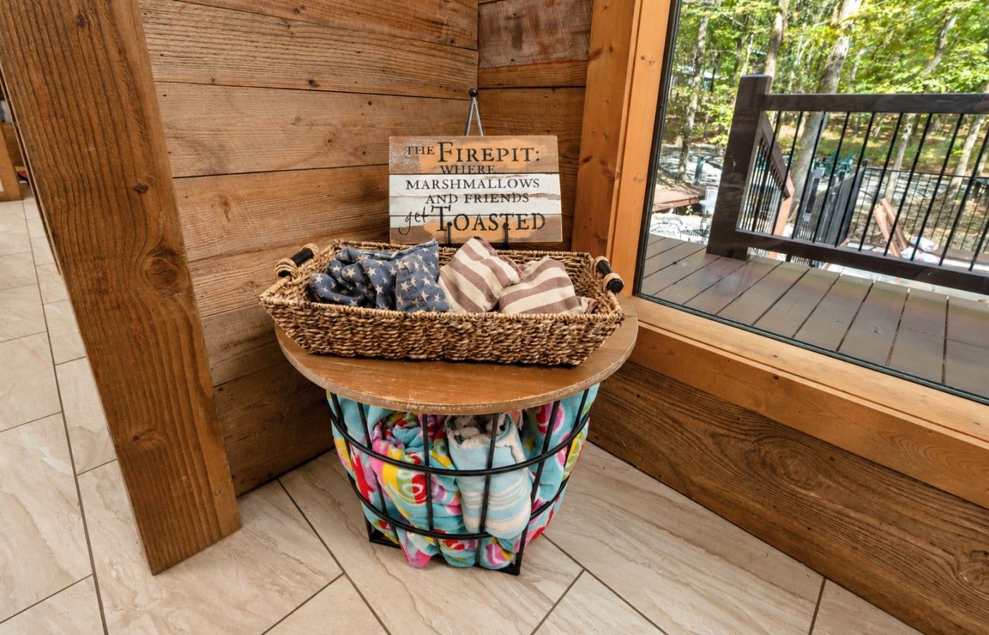 A corner of a room with a wooden wall, a wicker basket on a stool, and a sign that reads 'The Firepit: Marshmallows and Friends get Toasted.'