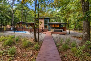 Une cabane avec une piscine, entourée d’arbres, et une terrasse en bois menant à l’entrée.