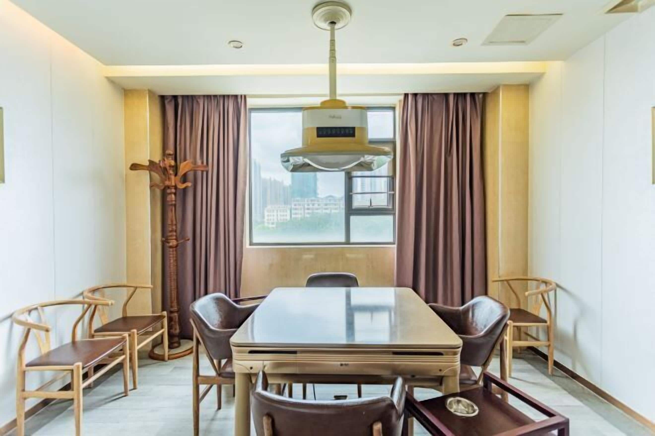 Une chambre d’hôtel avec une grande table à manger, quatre chaises, un grand lampadaire et une fenêtre avec des rideaux.