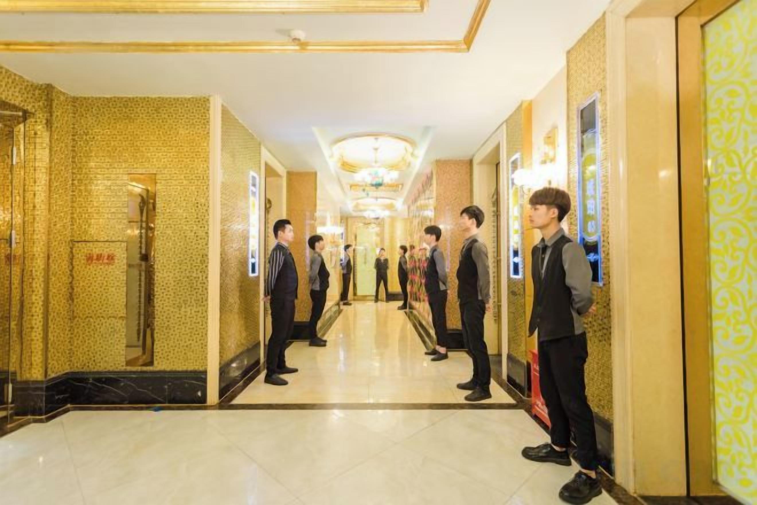 A hotel corridor with a mirrored wall, a reception desk, and a chandelier.