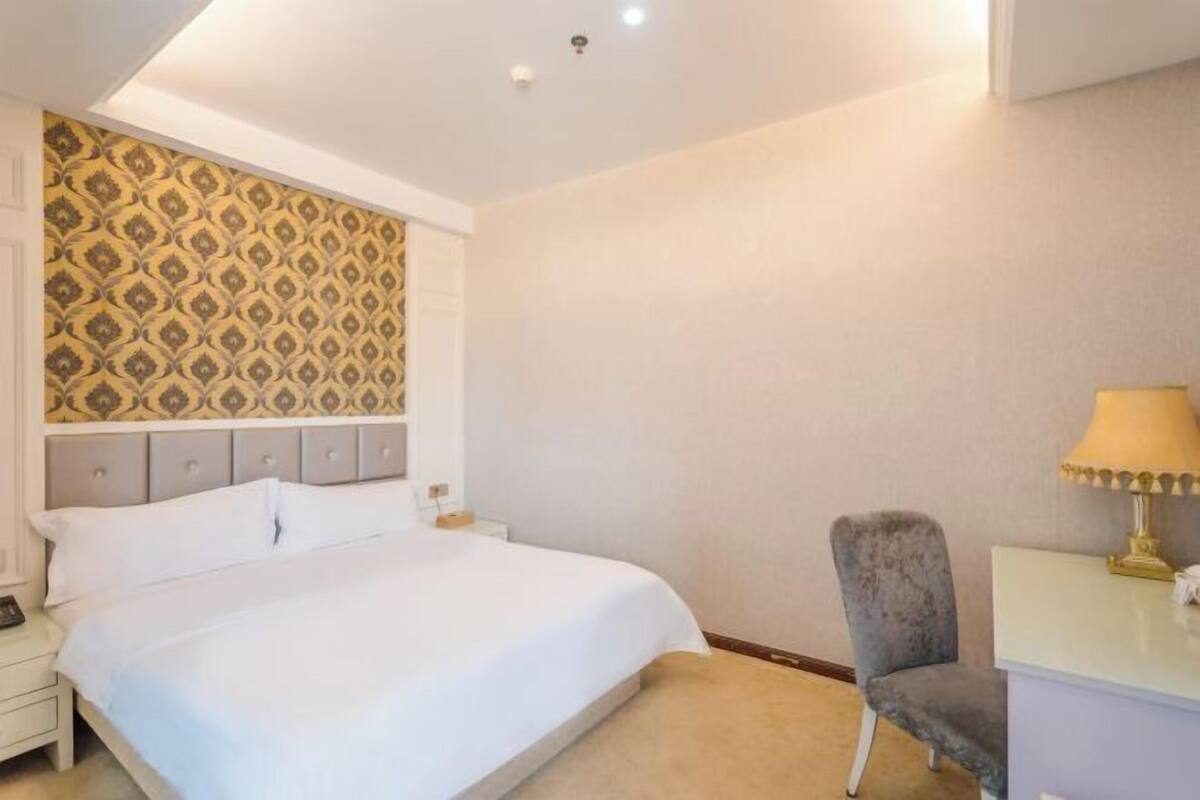 A hotel room with a large bed, a nightstand, a desk with a lamp, and a chair.
