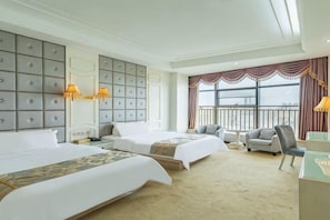A hotel room with two beds, a seating area with chairs, a desk, and large windows with curtains.