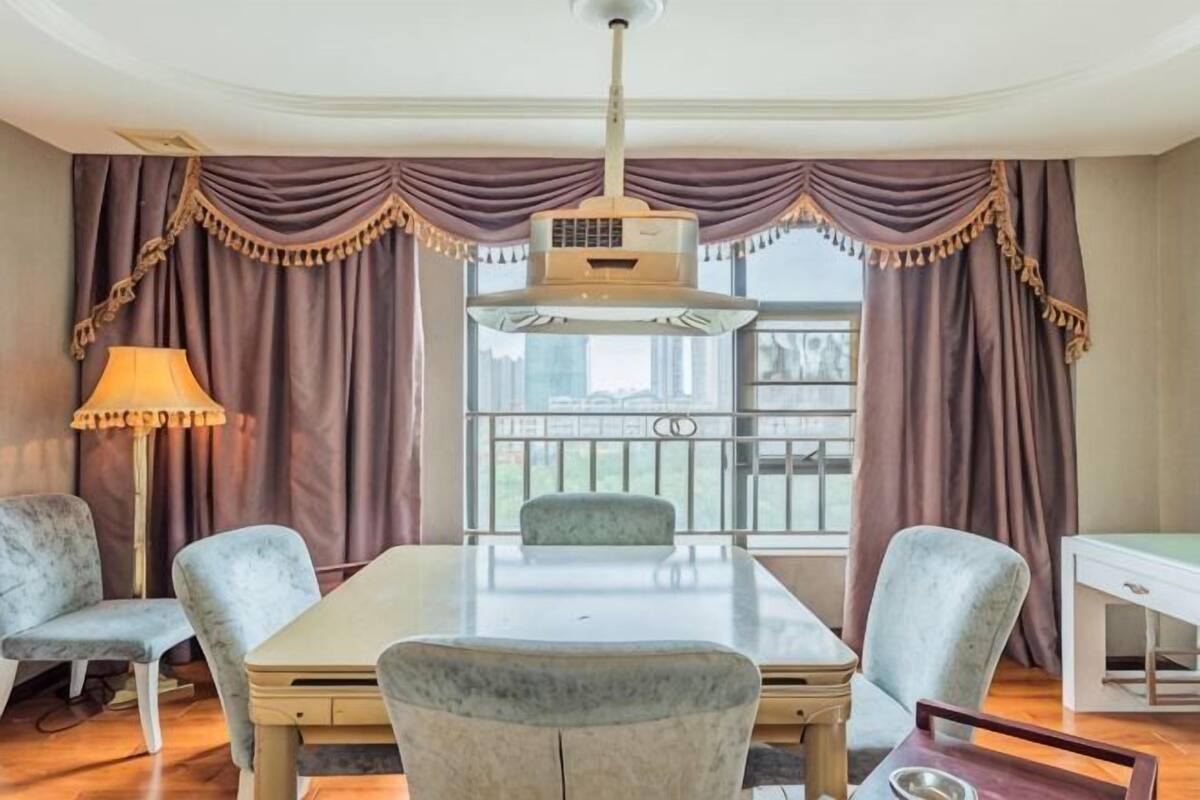 A dining area with a table, chairs, a lamp, and curtains.