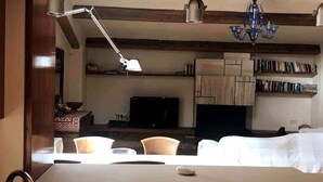 A modern kitchen with a dining area, wooden beams, a chandelier, and a flat-screen TV. - Duplex (Lloret de Mar)