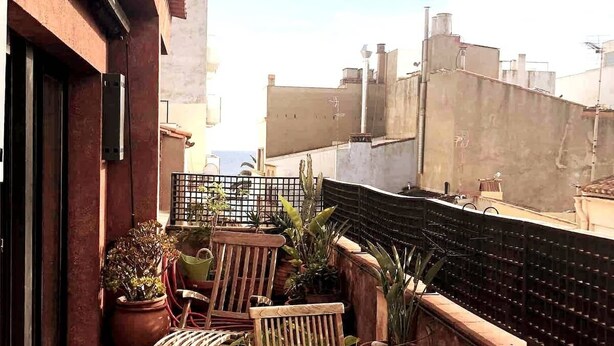 A rooftop terrace with a wooden table, chairs, potted plants, and a view of the cityscape. - Duplex (Lloret de Mar)