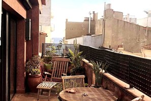Una terraza en la azotea con una mesa de madera, sillas, plantas en macetas y vistas de la ciudad.