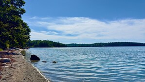 A clear view of a lake with a pebble beach and a forested island in the distance. - Lucky Stone Retreat - Private Beach & Acadia View (Sullivan)