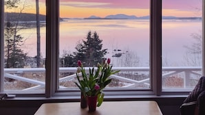 A view of a lake with mountains in the distance, a sunset, and a tulip vase on a windowsill. - Lucky Stone Retreat - Private Beach & Acadia View (Sullivan)