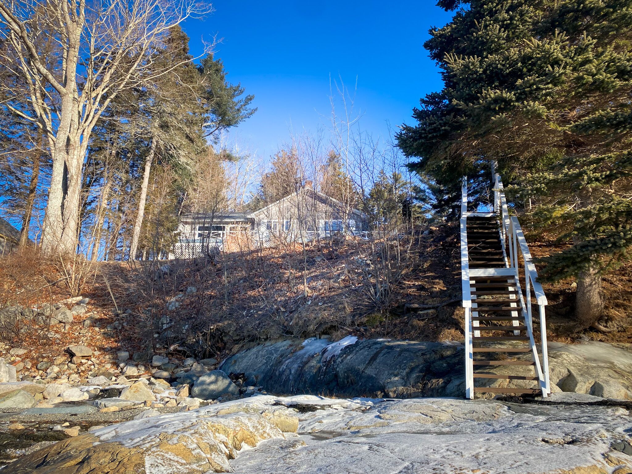 En trätrappa som leder upp till ett hus omgivet av träd och stenar.