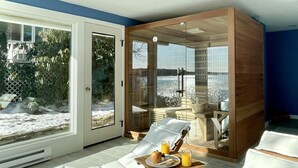 A sunlit room with a glass door leading to a snowy outdoor area, a wooden-framed seating area, and a table with breakfast items. - Lucky Stone Retreat - Private Beach & Acadia View (Sullivan)