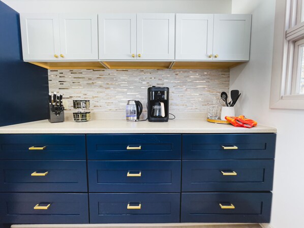 A kitchen with white cabinets, a coffee maker, a kettle, and a knife block. - Lucky Stone Retreat - Private Beach & Acadia View (Sullivan)