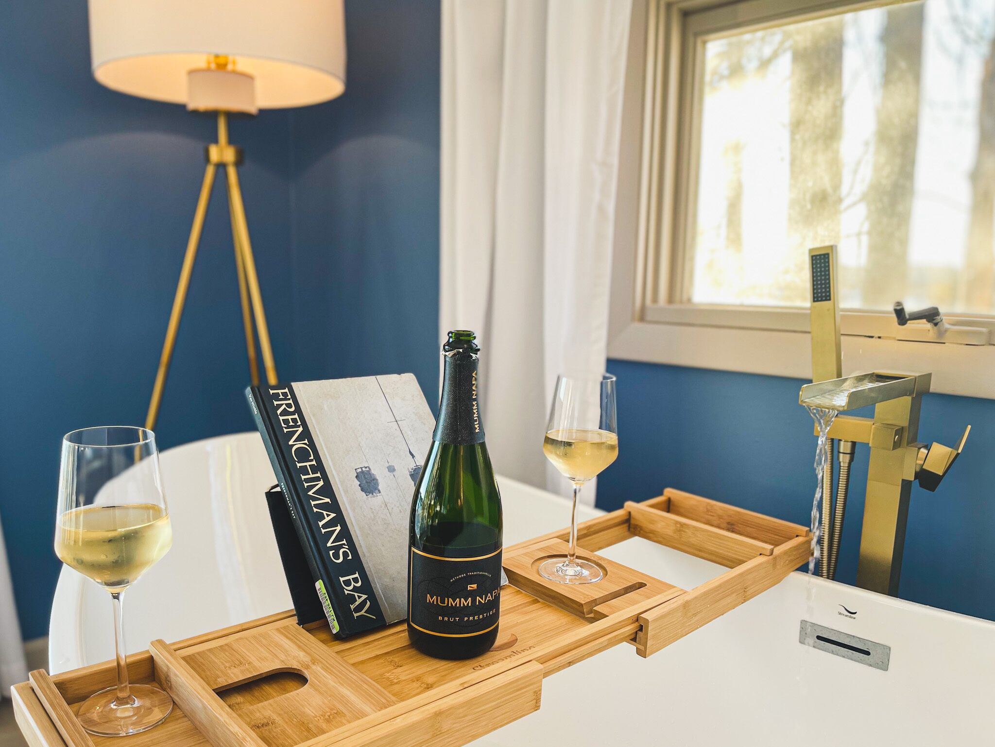 Un vassoio di legno con una bottiglia di spumante Mumm Napa Brut Prestige, un bicchiere di vino e un libro intitolato 