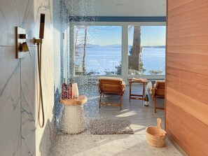 A modern bathroom with a glass-enclosed shower, wooden furniture, and a view of a snowy landscape. - Lucky Stone Retreat - Private Beach & Acadia View (Sullivan)