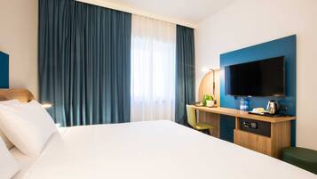 Habitación de hotel con una cama grande, un escritorio, un televisor de pantalla plana, una silla y una mesita con una planta y una botella.