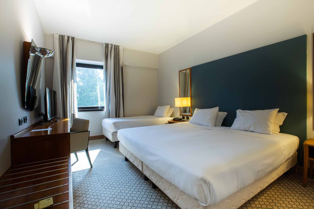 A hotel room with two beds, a desk, a chair, a TV, and a window with curtains.