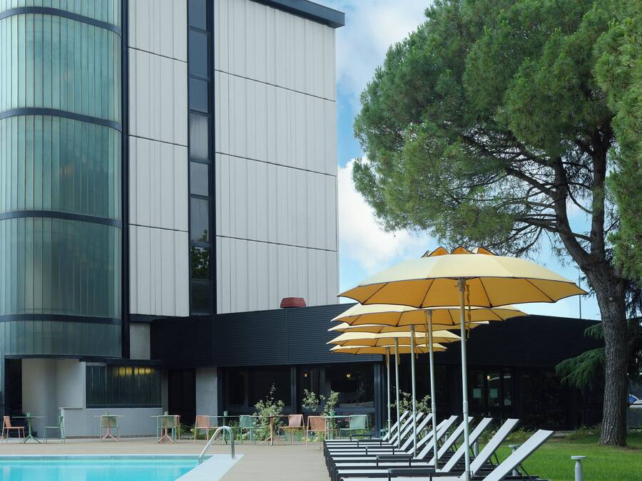 A modern hotel with a pool area, outdoor seating, and umbrellas.