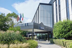A modern hotel entrance with a covered walkway, flags, and well-maintained landscaping. - Belstay Venezia Mestre (Mestre)