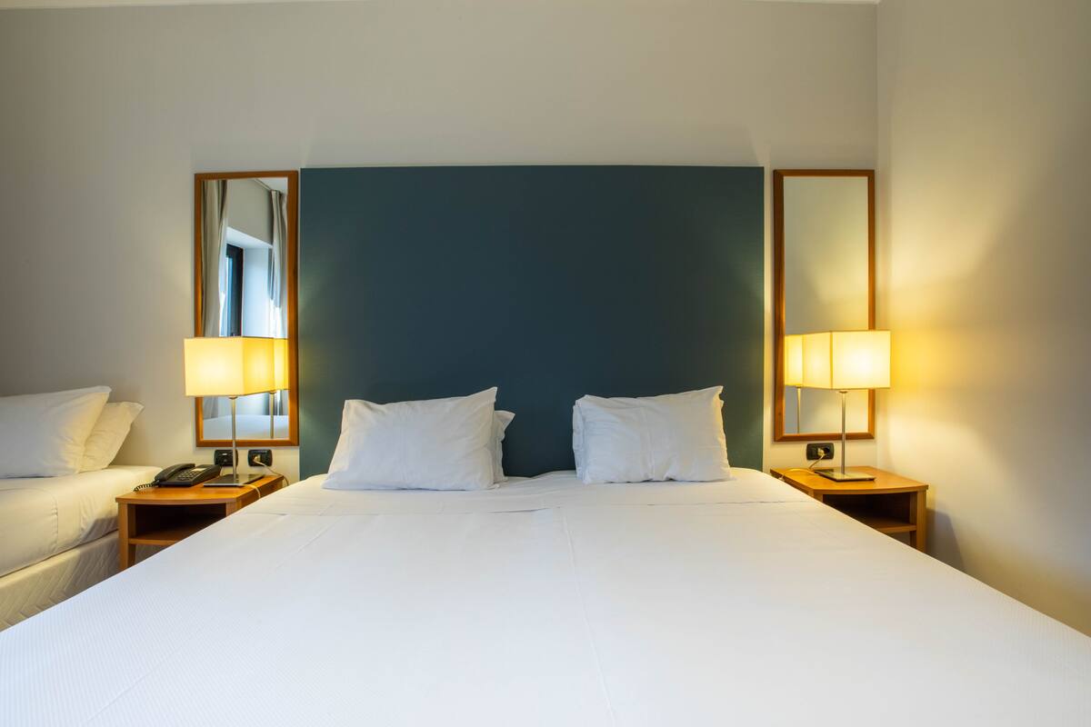 A hotel room with a large bed, two bedside tables with lamps, a mirror, and a window with curtains.