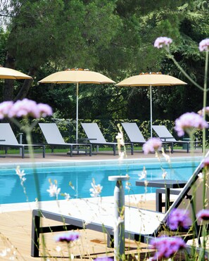 A poolside area with lounge chairs and umbrellas, surrounded by greenery. - Belstay Venezia Mestre (Mestre)