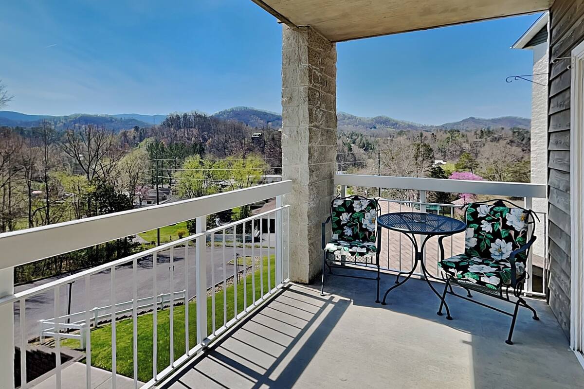 A balcony with a view of mountains, a table, and two chairs.