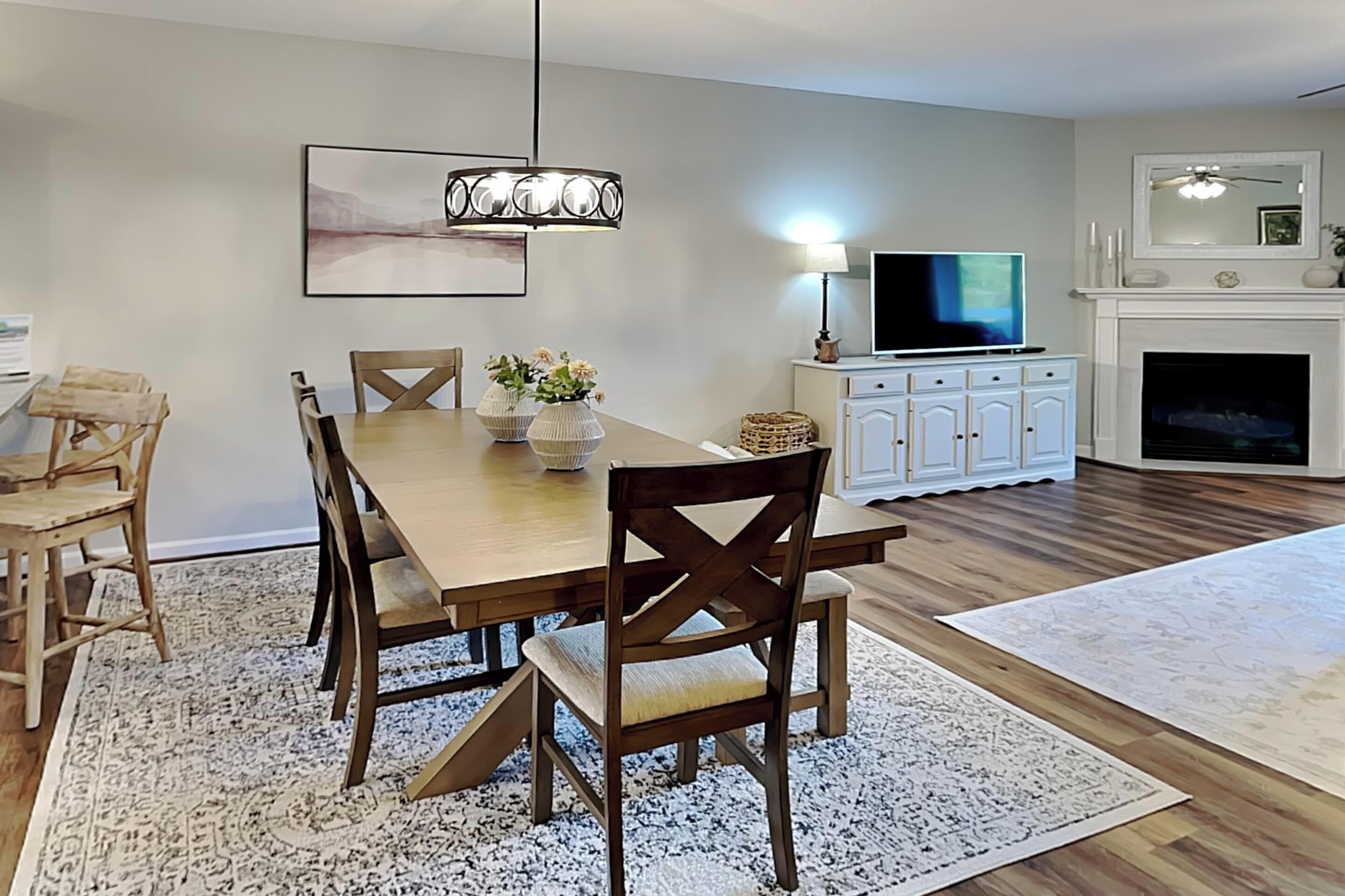 Un coin repas avec une table et des chaises en bois, un lustre et un téléviseur posé sur un meuble.