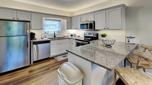 A modern kitchen with stainless steel appliances, white cabinetry, and a granite countertop. - Whispering Pines II by Jackson Mountain Rentals (Pigeon Forge)