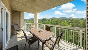 A balcony with a table and chairs, overlooking a forested landscape. - Whispering Pines II by Jackson Mountain Rentals (Pigeon Forge)
